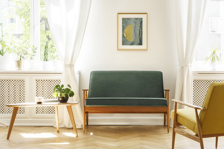 A mid-century living room interior with a sofa, coffee table, windows and painting